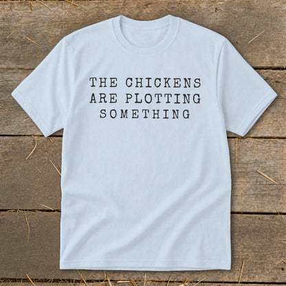 Light blue t-shirt with black text reading "THE CHICKENS ARE PLOTTING SOMETHING".