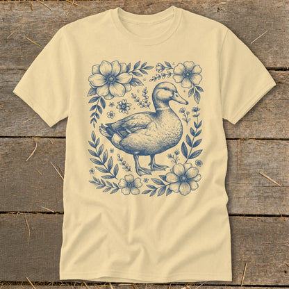 Light yellow t-shirt with a blue line drawing of a duck surrounded by flowers and leaves.