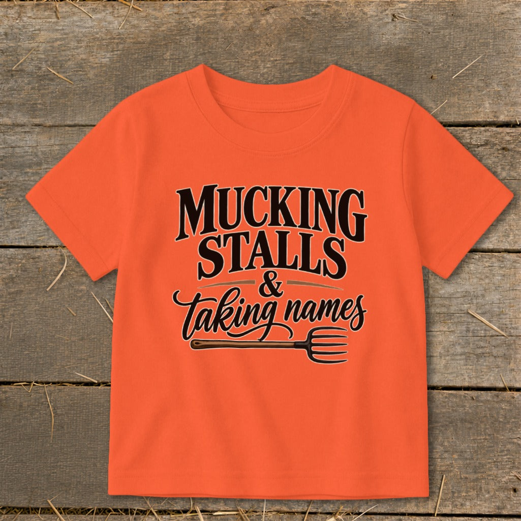 Orange t-shirt with text "Mucking Stalls & Taking Names" and a pitchfork.