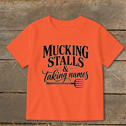 Orange t-shirt with text "Mucking Stalls & Taking Names" and a pitchfork.