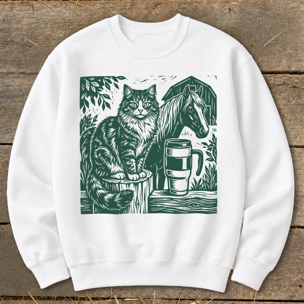 White sweatshirt with a green graphic of a cat, horse, and mug on a wooden surface.