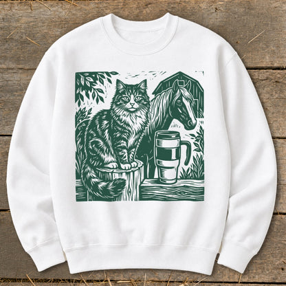 White sweatshirt with a green graphic of a cat, horse, and mug on a wooden surface.