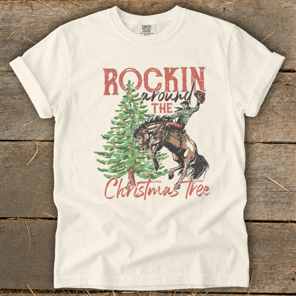 Cream t-shirt with "Rockin Around The Christmas Tree" graphic of a cowboy on a bucking horse.