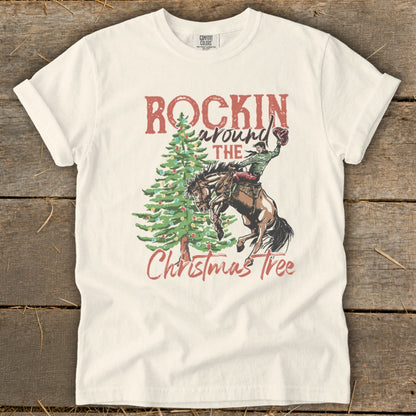 Cream t-shirt with "Rockin Around The Christmas Tree" graphic of a cowboy on a bucking horse.