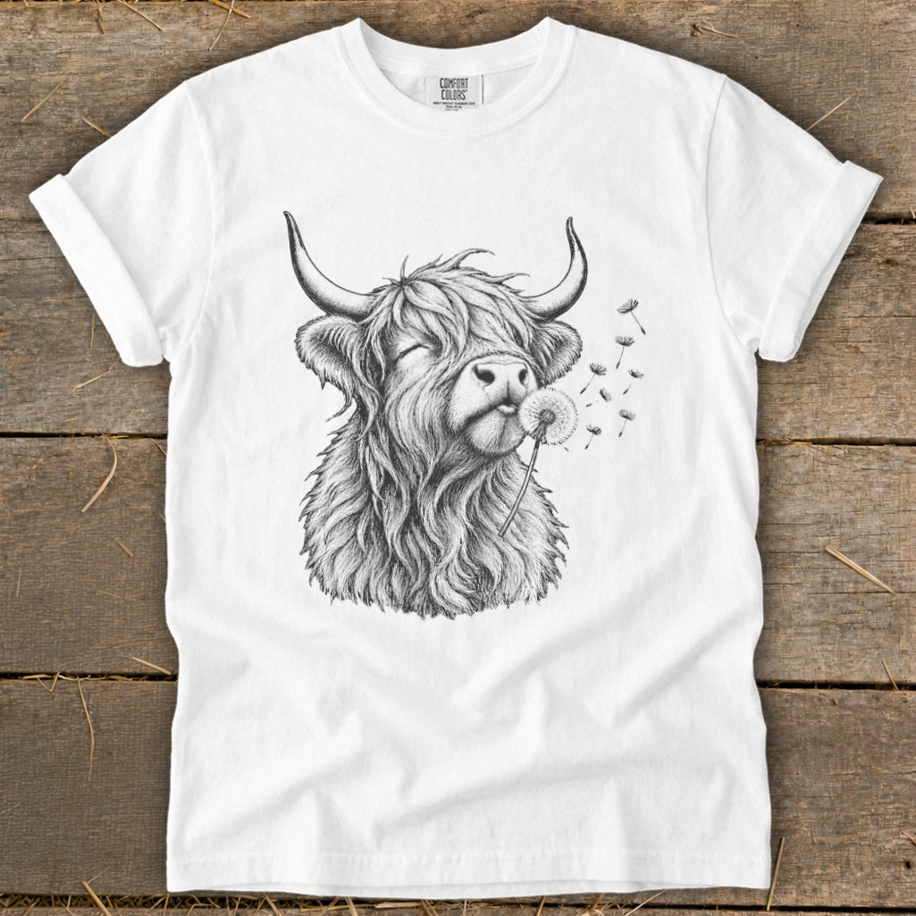 White t-shirt with a sketch of a Highland cow blowing on a dandelion.