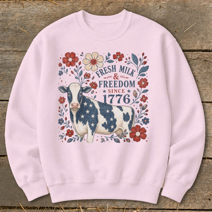 Pink sweatshirt with a patriotic cow and floral design, featuring text "Fresh Milk & Freedom Since 1776".