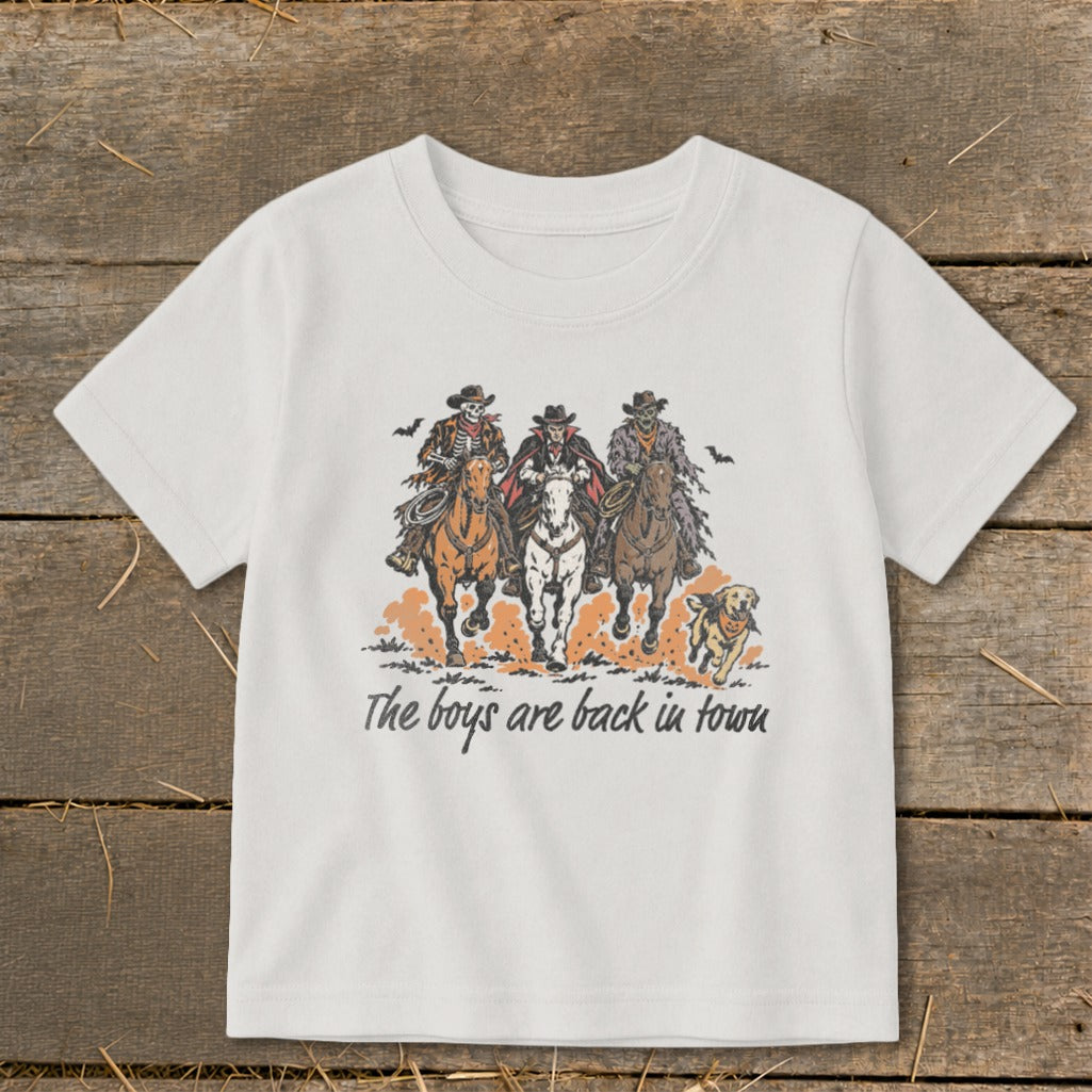 Three skeletal cowboys and a dog ride horses with text "The boys are back in town".