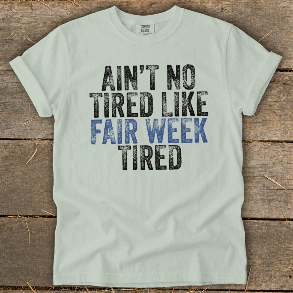 Light green t-shirt with black and blue text that reads "Ain't No Tired Like Fair Week Tired".