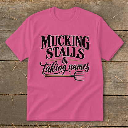 Pink t-shirt with text "MUCKING STALLS & taking names" and a pitchfork graphic.
