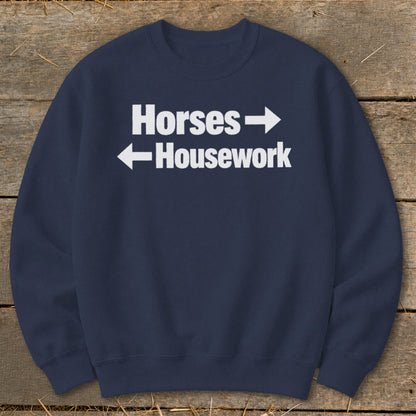 Navy blue crewneck sweatshirt with white text reading Horses with a right arrow above Housework with a left arrow.