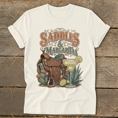 T-shirt graphic with text "Saddles & Margaritas," showing a saddle, margarita, and desert plants.