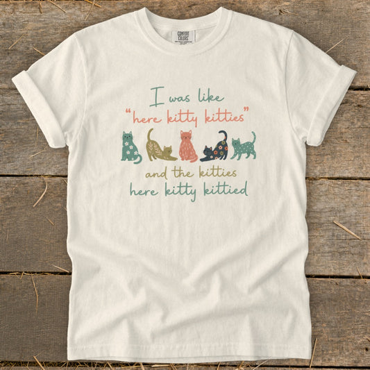White t-shirt with "I was like 'here kitty kitties' and the kitties here kitty kittied" and cat illustrations.