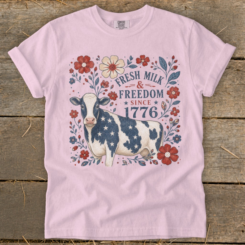 Pink t-shirt with a cow on American flag pattern and text "Fresh Milk & Freedom Since 1776".