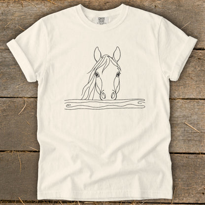 Minimalist line art of a horse's head peeking over a wavy line on a cream t-shirt.