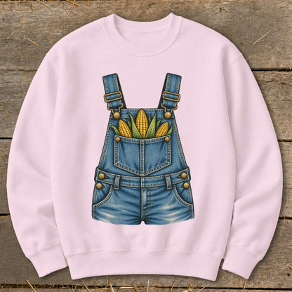 Pink sweatshirt with a graphic of denim overalls filled with corn on the cob.