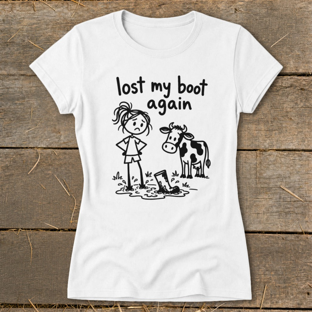 A white short-sleeved t-shirt featuring a cartoon graphic of a sad girl and a cow standing near a muddy boot, with the text "lost my boot again".