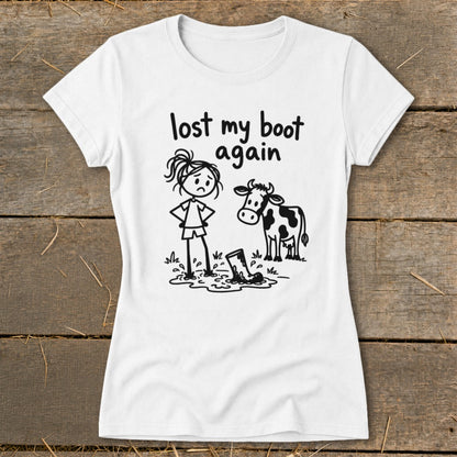 A white short-sleeved t-shirt featuring a cartoon graphic of a sad girl and a cow standing near a muddy boot, with the text "lost my boot again".