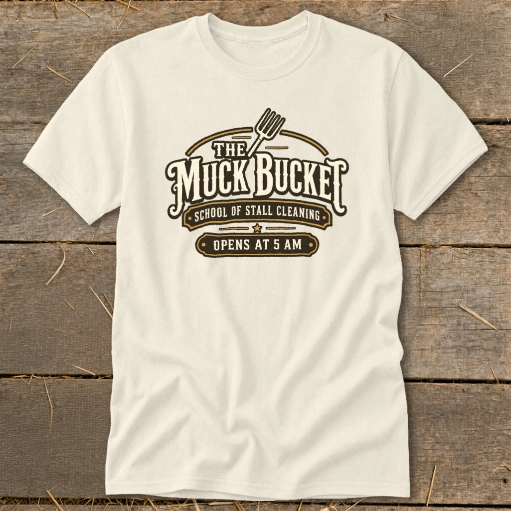 Cream t-shirt with "The Muck Bucket School of Stall Cleaning Opens at 5 AM" graphic.