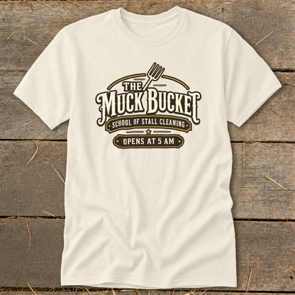 Cream t-shirt with "The Muck Bucket School of Stall Cleaning Opens at 5 AM" graphic.