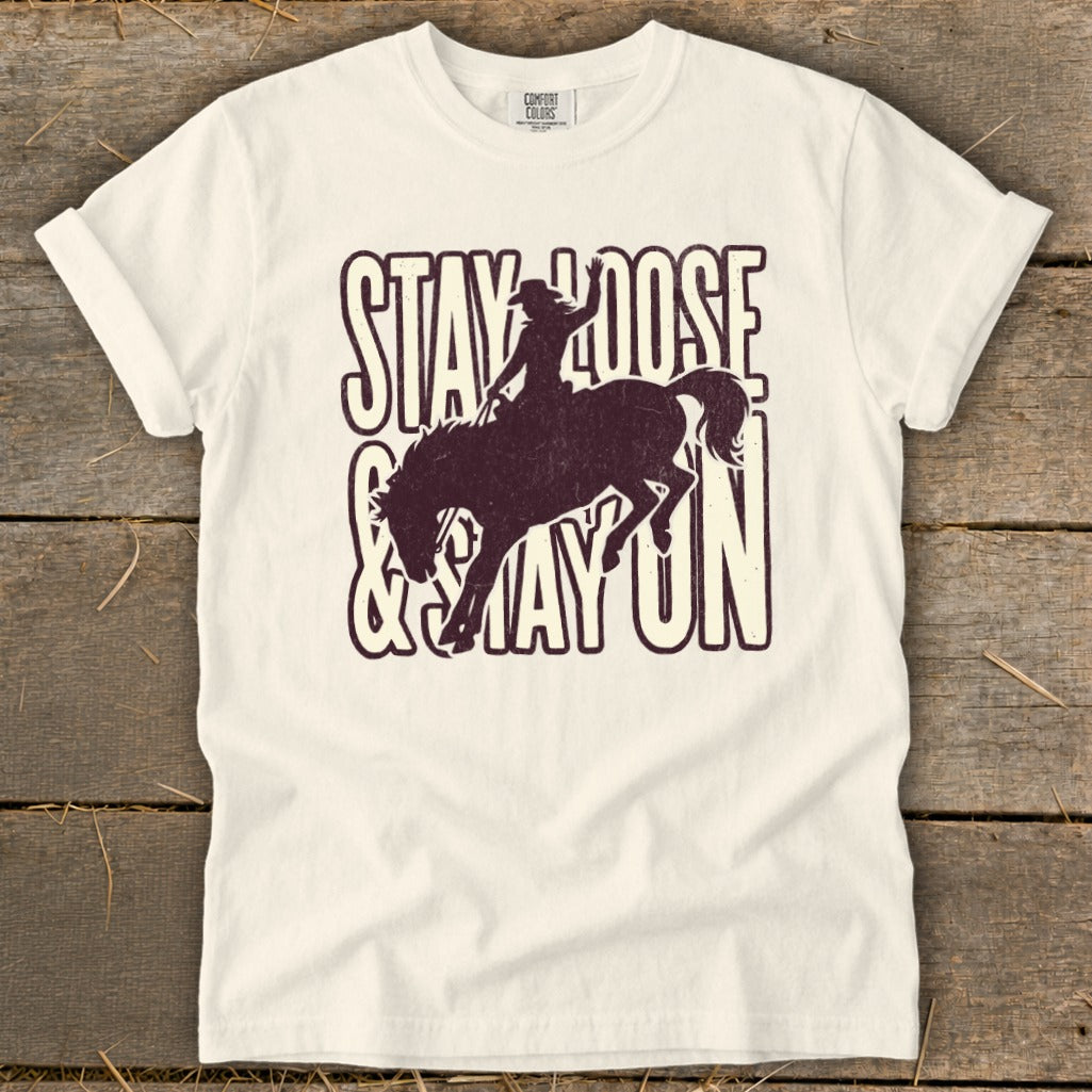Cream t-shirt with distressed print of a bucking bronco rider and text "Stay Loose & Stay On".