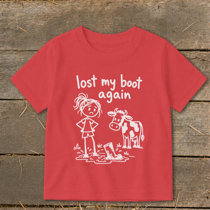 Red children's t-shirt featuring a white line drawing of a sad girl standing next to a cow by a muddy boot with the text "lost my boot again".