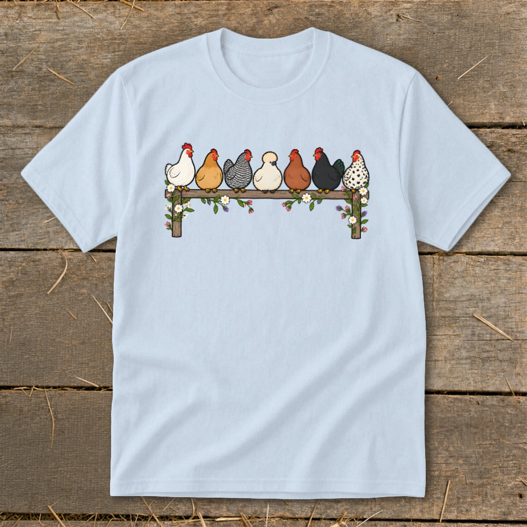 Light blue t-shirt featuring an illustration of seven colorful chickens sitting on a flower-decorated wooden fence.