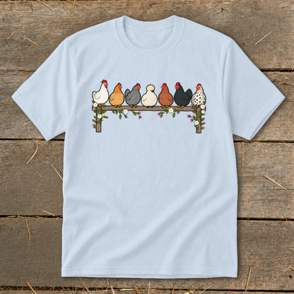 Light blue t-shirt featuring an illustration of seven colorful chickens sitting on a flower-decorated wooden fence.