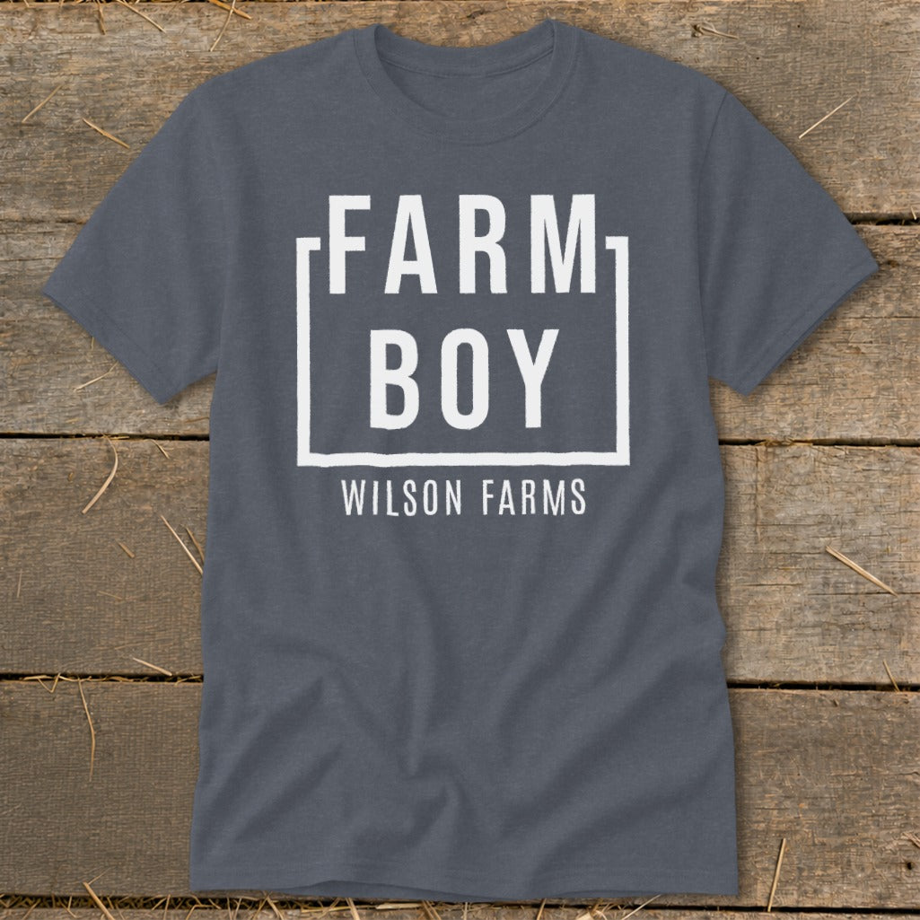 Dark grey t-shirt with white text "FARM BOY" inside a box and "WILSON FARMS" below.