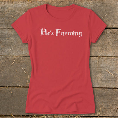 Red t-shirt with white text "He's Farming" on a wooden background.