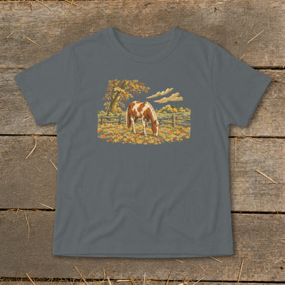 Brown and white horse grazing in a field of autumn leaves with a wooden fence.