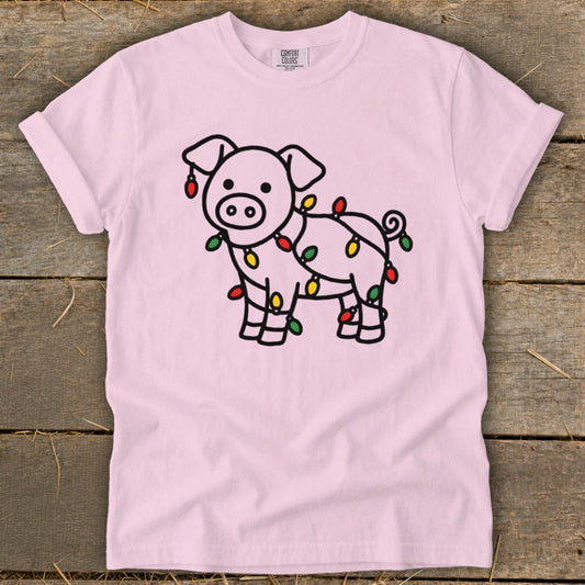 Light pink t-shirt featuring a line drawing of a pig tangled in colorful Christmas lights.