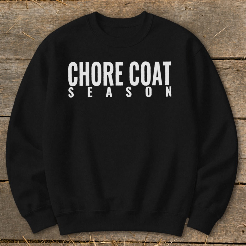 Black sweatshirt with white text "CHORE COAT SEASON" on a wooden background.