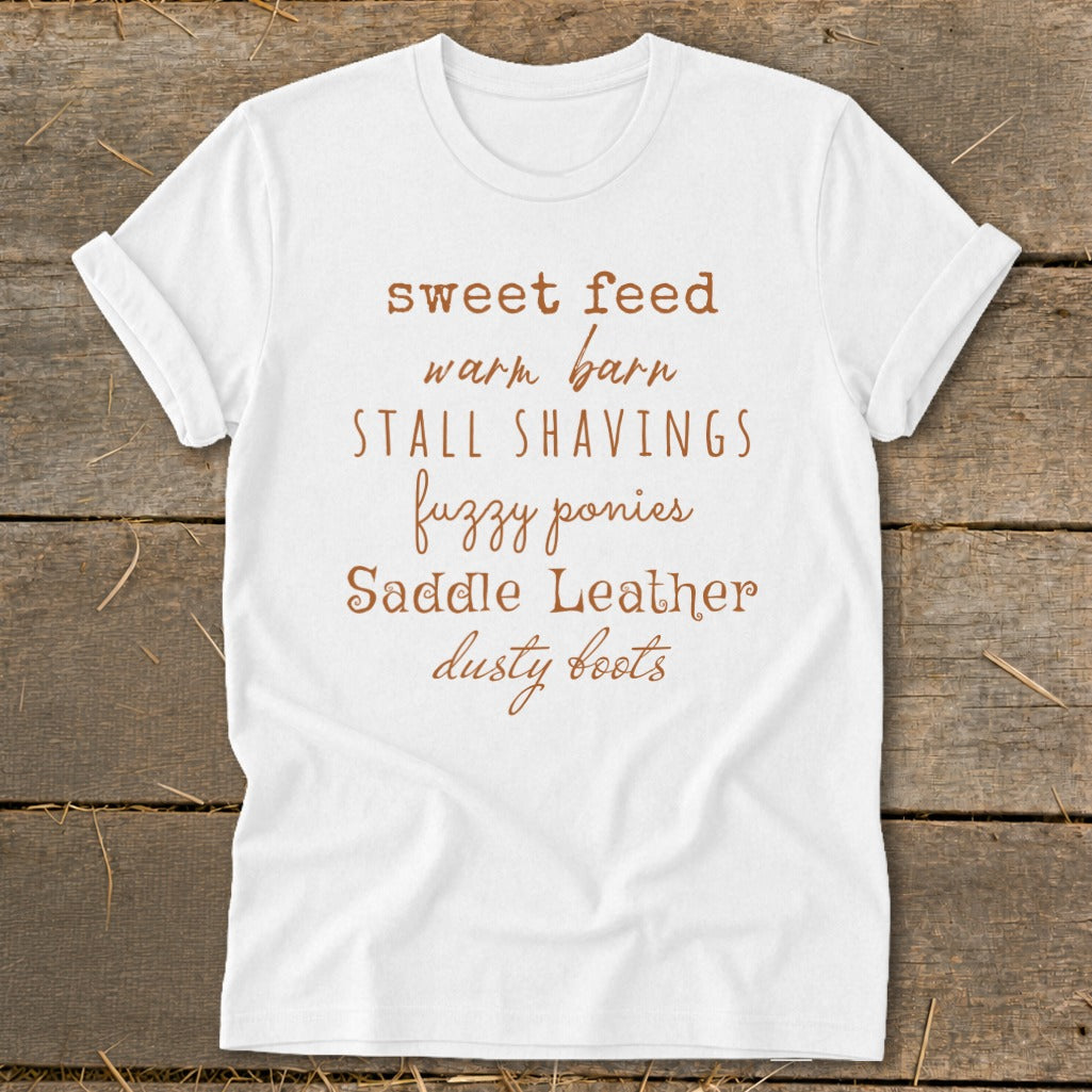White t-shirt with "sweet feed warm barn stall shavings fuzzy ponies saddle leather dusty boots" text.