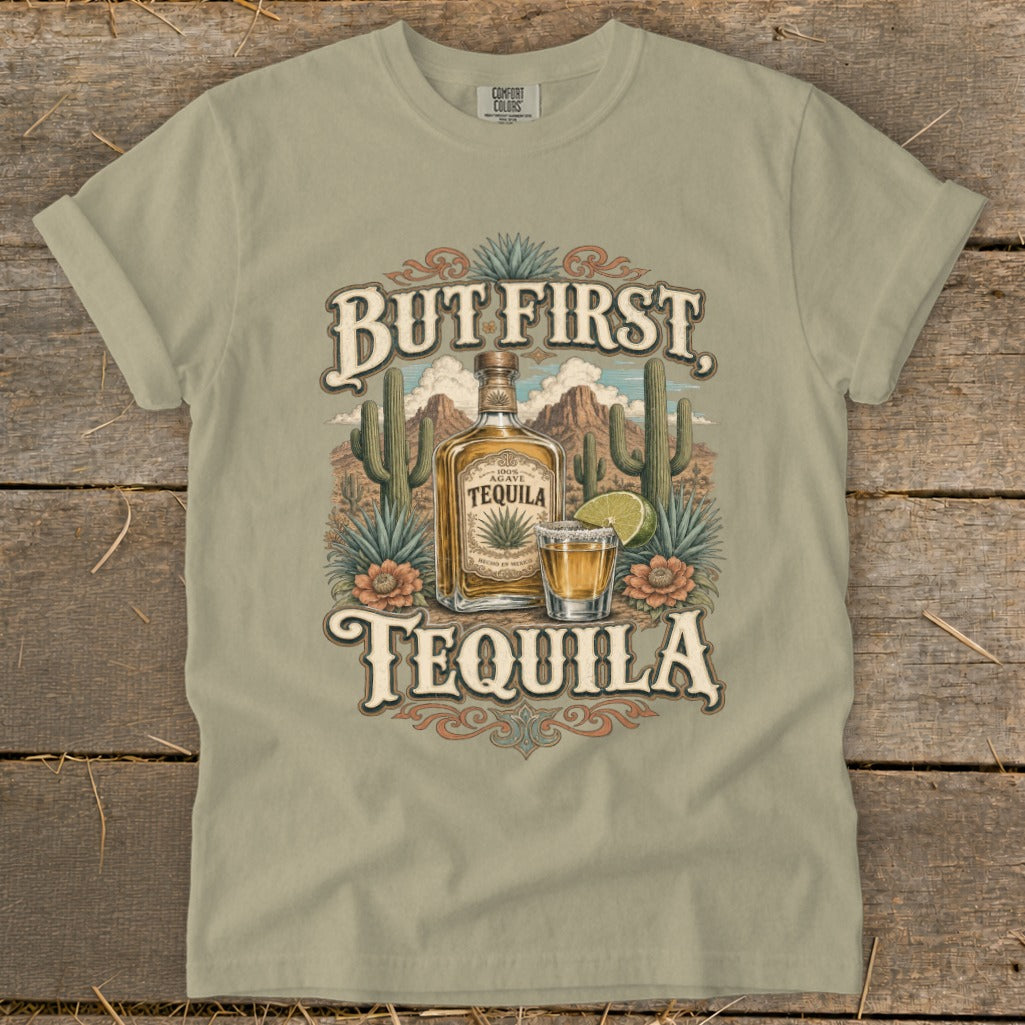 T-shirt graphic with "But First, Tequila" text, tequila bottle, shot glass, and desert scene.