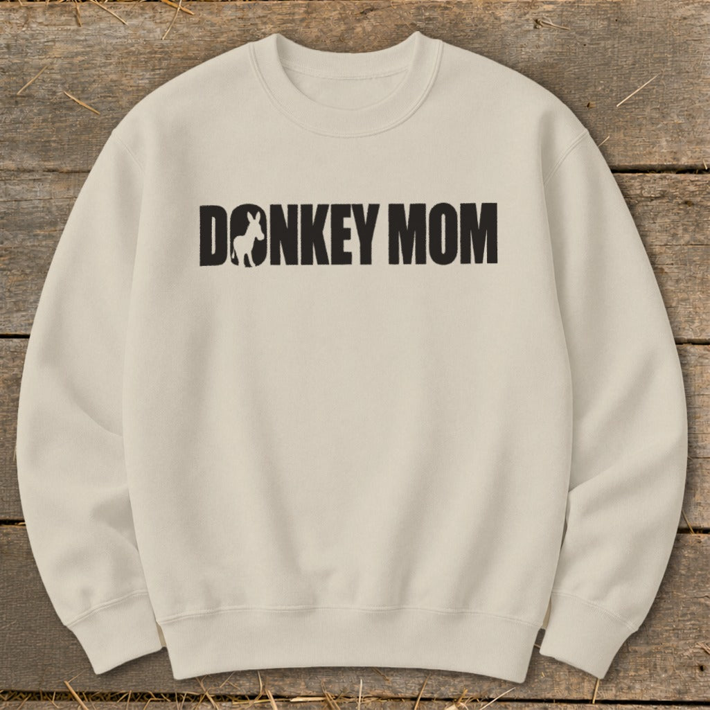 A cream-colored crewneck sweatshirt with the black text Donkey Mom centered on the chest.