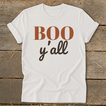 White t-shirt with brown text "BOO y'all" on a wooden background.