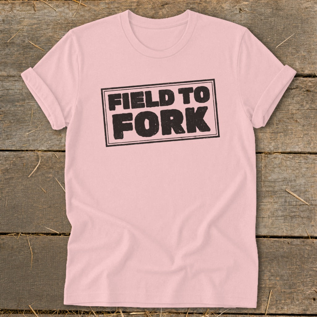Light pink t-shirt featuring a black rectangular stamp graphic with the text FIELD TO FORK.