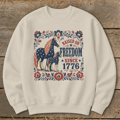 Cream sweatshirt with American flag horses and "Raised on Freedom Since 1776" text.