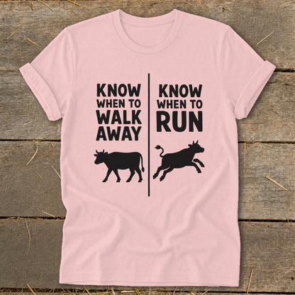 Pink t-shirt with black text "KNOW WHEN TO WALK AWAY" and a cow, and "KNOW WHEN TO RUN" and a running cow.