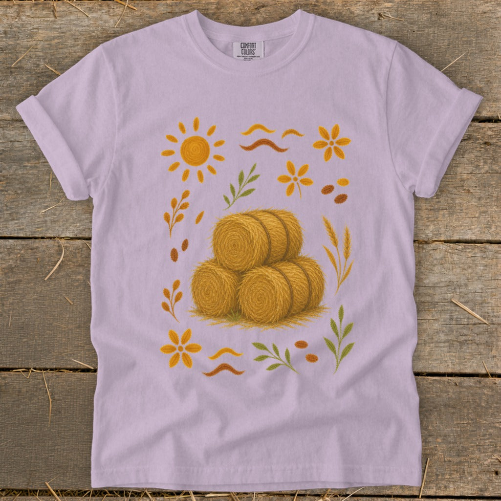 Light purple t-shirt with a scattered autumn harvest graphic featuring hay bales, sun, and leaves.