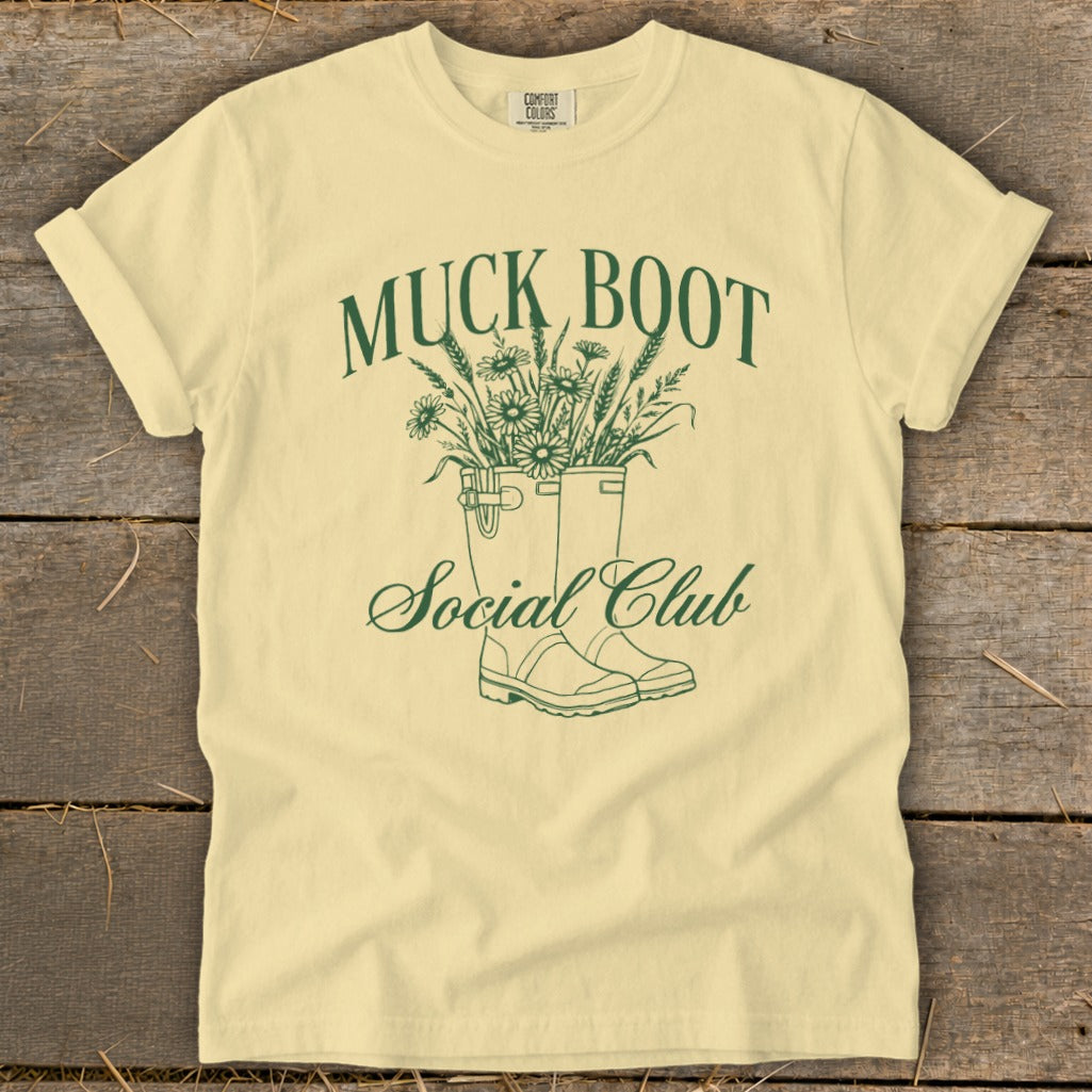 Yellow t-shirt with green text and graphic of muck boots filled with flowers.