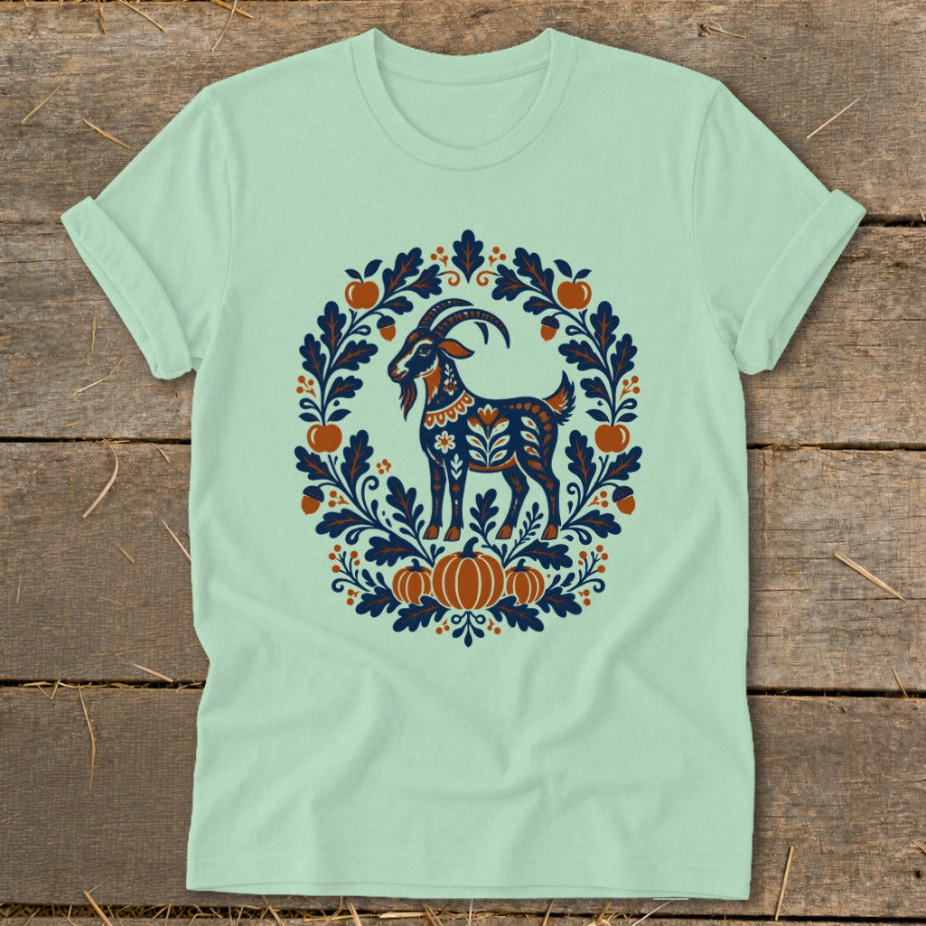 Light green t-shirt with a folk-art design of a blue goat inside an autumn wreath.