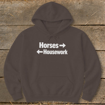 A dark brown hoodie featuring white text that reads Horses with a right arrow above Housework with a left arrow.