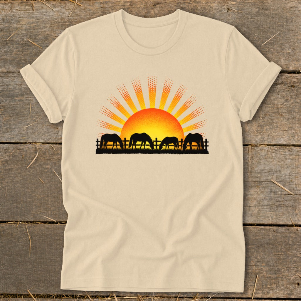 Four horses graze in silhouette before a rising sun over a fence.