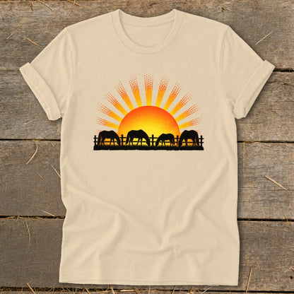 Four horses graze in silhouette before a rising sun over a fence.