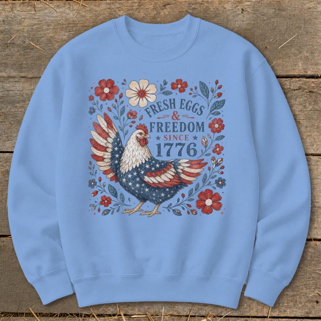 Light blue sweatshirt with a patriotic chicken and floral design, reads "Fresh Eggs & Freedom Since 1776".