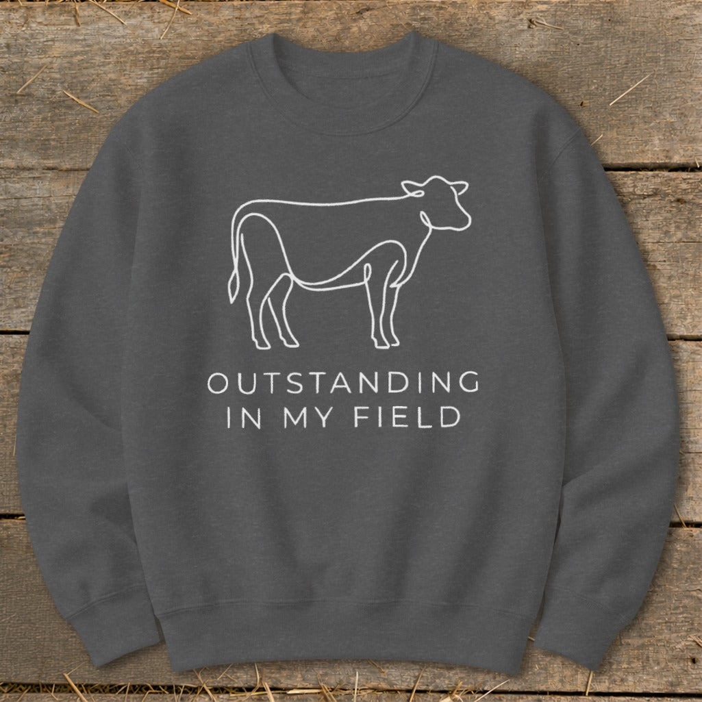 Dark grey sweatshirt with a white line drawing of a cow and text "OUTSTANDING IN MY FIELD".