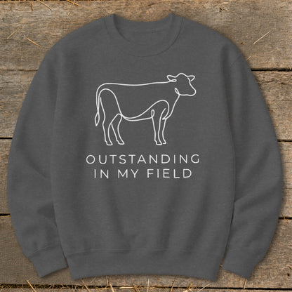 Dark grey sweatshirt with a white line drawing of a cow and text "OUTSTANDING IN MY FIELD".
