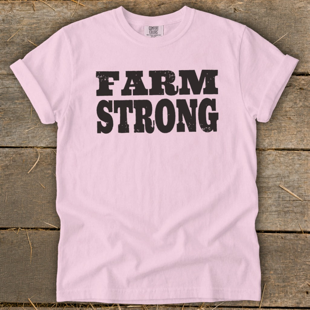 Light pink t-shirt with rolled sleeves featuring the bold black text FARM STRONG on a wooden background.