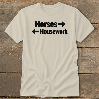 A cream-colored crewneck t-shirt with black text that reads Horses with a right arrow above Housework with a left arrow.